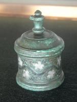 PYX-4017 - Pyxide
bronze
Pyxide cylindrique, au corps limité par des moulures; panse rectiligne ornée de motifs gravés et incrustés d'argent (argent); couvercle conique à bouton sommital pour la préhension.