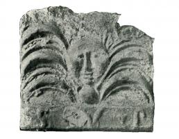 ANT-4005 - Antéfixe : Palmette à 7 branches sur têteterre cuiteTête (d'homme ou de lion) émergeant de palmes, parfois posée sur un globe et surmontant une marque épigraphique.