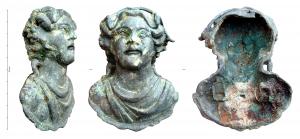APM-4030 - Applique : buste de Bacchusbronze, ferApplique en forme de buste juvénile aux traits réguliers, mais écarquillés, le buste couvert d'un vêtement plissé retenu sur l'épaule droite, et émergeant d'une courte corolle; les mèches de cheveux encadrent régulièrement le visage et sont surmontées d'un rinceau de vigne, dont les grappes pendent de part et d'autre du visage. Revers creux, avec l'arrachement de deux pitons de fixation en fer, de section rectangulaire.