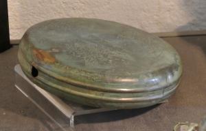 GRD-3001 - GourdebronzeGourde plate en tôle, de forme cylindrique aplatie, constituée de deux coques en tôle serties sur la tranche; un col rapporté est fixé sur une ouverture latérale circulaire.