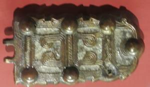 PLB-5593 - Plaque-boucle articuléebronzePlaque-boucle articulée à charnons, plaque rectangulaire ornée de caissons et de motifs évoquant des fils ou des tracés au peigne.