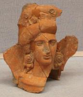 STE-3002 - Statuette : tête féminineterre cuiteFigurine de taille importante, en forme de tête féminine parée de bijoux (boucles d'oreilles, colliers...) et à la coiffure élaborée.