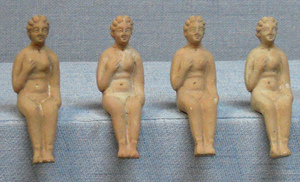 STE-3006 - Statuette : femme nue assiseterre cuiteFigurine moulée représentant une femme nue assise, au visage souriant encadré d'une chevelure coiffée en rouleaux; la main droite se porte sur le sein droit, la gauche reposant contre la cuisse.