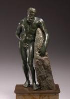 STE-4024 - Statuette : Héraklès - Hercule appuyé au rocher (variante)bronzeHercule sous la forme d'un homme d'âge mur, nu et à la puissante musculature, déhanché vers la droite, s'appuie à gauche sur un rocher, la main droite dans le dos, la tête penchée vers le sol.