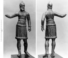 STE-4497 - Statuette : Jupiter DolichenusbronzeDivinité sous la forme d'un homme d'âge mur, barbu, casqué et portant une cuirasse musclée sur un vêtement dont les plis transversaux parallèles peut évoquer le costume oriental. Sous les pieds, tenons pour fixation sur une figurine de bovidé.