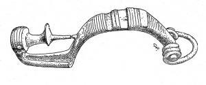 FIB-2054 - Fibule à tête d'oiseau ('Vogelkopffibel')bronzeTPQ : -475 - TAQ : -400Fibule coulée, dont le pied redressé figure une tête d'oiseau aquatique (anatidé), au large bec en spatule (ouvert ou fermé); œil généralement inscrutsé, de même que l'arc épais, qui est creusé d'encoches transversales, ou longitudinales, pour insertion de bâtonnets de corail. La tête de l'arc est perforée pour le montage d'un ressort court, sur axe.