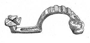 FIB-2637 - Fibule à pied redressé et arc orné de corailbronzeFibule coulée, dont le pied redressé à angle droit se termine par une plaque carrée, incisée en croix ; l'arc, épais, est creusé d'encoches transversales pour insertion de bâtonnets de corail. La tête de l'arc est perforée pour le montage d'un ressort court, sur axe.