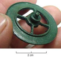 FIB-4462 - Fibule skeuomorphe : rouebronzeTPQ : 100 - TAQ : 260Fibule en forme de roue : le moyeu est représenté, plein, non émaillé, avec l'extrémité de l'essieu (?) ainsi que 4 rayons seulement, et la jante lisse.