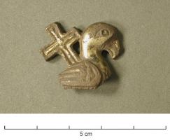 FIB-5115 - Fibule zoomorphe : oiseau et croixbronzeTPQ : 700 - TAQ : 900Oiseau (colombe, paon...?) stylisé de profil à droite, les ailes repliées, surmonté d'une croix. Décor en relief plat ciselé. Ressort et ardillon en fer sur charnière à plaquette.