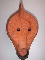 LMP-4583 - Lampe Hayes II : Eveterre cuiteLampe africaine tardive classique. Médaillon orné d'une femme se tenant les cheveux : Eve? Epaule ornée de motifs géométriques. Argile orange, engobe orange. Anse à l'arrière.