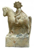 STE-4081 - Statuette : Sol enfantterre cuiteFigurine représentant, sur un socle quadrangulaire haut et lisse, Sol enfant, sous la forme d'un jeune garçon à tête radiée, vêtu d'un seul manteau de cavalier, montant à cru un petit cheval harnaché. Le dieu tourne la tête vers la gauche pour faire face au spectateur.