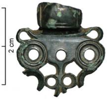 AGH-4001 - Agrafe de harnaisbronzeAgrafe de harnais coulée, comportant un robuste anneau et une plaque antérieure à bord festonné, percée de quatre orifices (ou davantage), entourés de cercles pour ceux qui servent à la fixation sur le cuir.