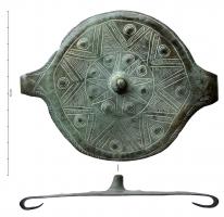 APP-1013 - Applique de ceinture circulairebronzeTPQ : -1250 - TAQ : -950Applique constituée d'une plaque circulaire en tôle, martelée à partir d'une pointe conique massive, avec deux ailettes repliées vers l'arrière pour la fixation. Décor rayonnant incisé, composé de triangles et de bossettes repoussées, motifs hachurés.