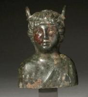 BLS-4023 - Balsamaire en forme de bustebronzeTPQ : 150 - TAQ : 300Vase plastique en forme de buste d'un jeune homme à la poitrine nue, parfois drapée d'une peau de bête. Chevelure bouclée au sommet de laquelle est découpée une ouverture circulaire fermée par un couvercle à charnière. Anneaux fixes soudées dans la chevelure supportant une poignée parfois disparue.