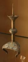 CHL-6002 - Chandelier émaillébronze doréTPQ : 1200 - TAQ : 1350Chandelier composite, formé d'éléments sertis sur un axe vertical, à partir d'un piètement tripode dont les pieds sont reliés par des plaques triangulaires, couvertes de motifs émaillés champlevés. La hampe est interrompue par une ou deux bagues globulaires, également émaillées, et le sommet consiste en une coupelle conique ou à bord horizontal, orné de fleurons, et une pique sommitale pour fixer une chandelle.