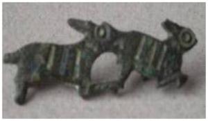 FIB-41553 - Fibule zoomorphe, groupe : chien et lièvrebronzeTPQ : 80 - TAQ : 120Broche plate, étamée, le corps strié de bandes parallèles étamées : chien poursuivant un lièvre à droite.