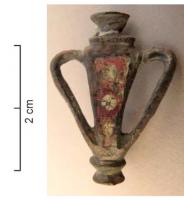 FIB-41566 - Fibule skeuomorphe émaillée : amphorebronzeTPQ : 120 - TAQ : 250Fibule émaillée, au coups triangulaire creusée d'une loge d'émail avec inclusion de millefiori; deux anses surélevées, un col d'un côté et un pied mouluré de l'autre, achèvent de donner à cette broche l'aspect d'une amphore au corps effilé.