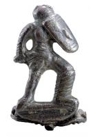 FIB-41776 - Fibule anthropomorphe : gladiateurargentTPQ : 100 - TAQ : 300Fibule représentant un gladiateur (myrmillon), en position de combat, le bouclier relevé au niveau du visage et le glaive horizontal, pointé vers l'adversaire ; au revers, articulation à ressort sur une longue corde externe, retenue par une griffe.