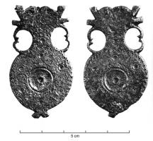 FRT-4012 - Ferret de ceinturebronzeFerret en forme d'amphore, de facture légère, anses découpées en peltes; panse circulaire, ornée d'un cercle central entouré de cercles oculés, bordures de plus petits cercles; double fleuron à la base.
