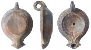 LMP-41524 - Lampe à bec triangulaire et volutes ébauchéesterre cuiteLampe moulée,anse verticale à deux sillons sur la tranche. Réservoir circulaire de profil convexe. Bandeau penché vers l'extérieur portant une couronne de feuilles Disque en cuvette, limité par un fin bourrelet et deux cercles concentriques en relief . Bec triangulaire à volutes simples ébauchées sur le bandeau. Trou d'évent sur un pseudo canal. Base circulaire plate en relief.  Engobe marron foncé .