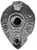 LMP-4197 - Lampe syro-palestinienne tardive terre cuiteTPQ : 400 - TAQ : 700Lampe de type pantoufle. Epaule décorée de cercles en relief.  Bec intégré dans la lampe et surmonté d'un canal, sur lequel se trouve un motif végétal. Anse conique.