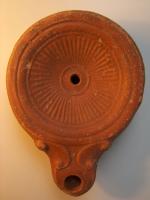 LMP-4313 - Lampe Loeschcke IV : Rosetteterre cuiteTPQ : 50 - TAQ : 150Lampe à bec à ogive et volutes latérales; disque orné de rayon ornant tout le médaillon ; base plate définie par un cercle incisé.