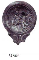 LMP-4760 - Lampe Loeschcke IV : Gladiateurterre cuiteTPQ : 50 - TAQ : 100Lampe ronde à large bec en ogive à volutes (cassé). Médaillon décoré d'un gladiateur (samnite) blessé, assis.
