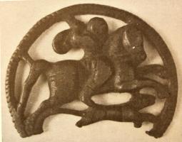 MRS-5006 - Applique latérale de morsbronzeApplique circulaire au pourtour lisse, avec une bélière rectangulaire au sommet pour la fixation des sangles. Le décor ajouré figure un cavalier à droite, sur son cheval cabré.