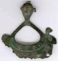 PDQ-2047 - PendeloquebronzeTPQ : -600 - TAQ : -475Pendant en forme de lunule (bateau ...?) avec deux extrémités redressées et pourvues de têtes divergentes, surmonté d'un triangle évidé avec au sommet une tête humaine surmontée d'un anneau de suspension. Perforations aux oreilles et à la base de la lunule pour de nombreux pendants annexes. La surface est ornée de cercles oculés.