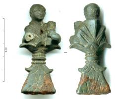 SPC-4021 - Spatule à cire : buste de magister ?bronzeManche en forme de buste d'homme, au crâne dégarni, vêtu d'un cucullus et tenant une theca calamaria dans les mains; l'extrémité distale montre une base plate, accostée d'ergots et ornée de plumes incisées, fendue dans l'épaisseur et coulée sur la lame de fer.