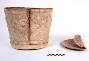 URN-4019 - Urne cylindrique à décor mouléplombUrne cylindrique en plomb à décor de rinceaux. La partie supérieure du cylindre est dotée d'une moulure formant une alternance d'un listel plat, de gorges, d'un quart de rond et d'une gorge égyptienne inversée. La partie inférieure du cylindre est décoré d'une moulure de perles en boudin et pirouettes fines. La panse a été coulée dans un moule permettant d'obtenir un décor moulé qui se développe sur tout le pourtour, une fois le vase refermé par une soudure ; fond circulaire rapporté ; un couvercle débordant, parfois orné d'un médaillon rapporté, peut compléter l'objet.