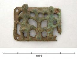 BAC-6005 - Boucle à chape ajourée rivetée : Adam et Eve autour de l'Arbre de ViebronzeBoucle à double fenêtre, chape rectangulaire ajourée et rivetée aux angles; le décor en relief plat, sauf les têtes en haut-relief, figure un homme et une femme (Adam et Eve), de part et d'autre d'un arbre.