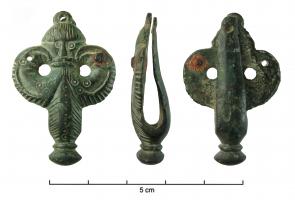 BOF-5005 - Bouterolle de fourreaubronzeTPQ : 450 - TAQ : 625Bouterolle trifoliée avec un visage humain au centre, flanqué de deux oiseaux se faisant face. On note un bouton à la base.