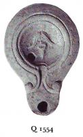 LMP-4775 - Lampe Loeschcke V Masqueterre cuiteTPQ : 90 - TAQ : 150Lampe à bec en ogive, accostée de volutes simples massive reliée au médaillon par un canal étroit où un sillon en demi-cercle est inscrit. L'épaule, convexe, est large, lisse et séparée du médaillon par un large bourrelet. Le médaillon est orné d'un masque de théâtre à cheveux long et barbe en pointe. Le fond est plat, dégagé par un sillon et peut comporter une marque en creux.