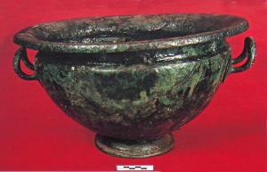 BAS-3001 - Bassin campanienbronzeBassin à panse hémisphérique profonde, col étranglé et lèvre nettement déversée vers l'extérieur ; pied étroit rapporté ; une paire d'anses fixées au sommet de la panse, redressées vers le haut.
