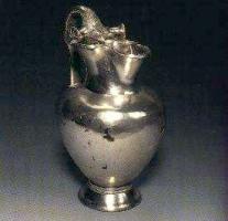 CRU-2004 - CrucheargentOenochoé à embouchure trilobée, anse légèrement surélevée, col vertical nettement séparé d'une panse ovoïde, lisse; piédouche orné d'incisions. L'essentiel du décor se concentre sur l'anse, accostée de deux disques verticaux sur la lèvre, ornée d'une dépouille de lion à la base.