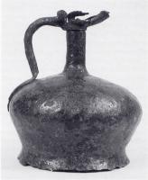 CRU-4068 - Cruche à profil sinusoïdalferCruche compose de plusieurs éléments assemblés et soudés : un corps cylindrique, formé d'un rectangle replié sur lui-même, le joint pouvant être couvert par l'anse rapportée; un fond circulaire plat, équipé de trois pieds parallélépipédiques; un col tronconique, parfois à degrés; et un bloc anse-col, parfois avec un couvercle articulé.