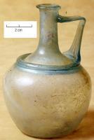 CRU-4087 - Cruche à épaulement marqué d'un ressautverreCruche en verre bleu-vert, soufflée à la volée, présentant une panse pommiforme décorée d'un anneau creux au niveau de l'épaulement. Fond plat, légèrement concave. Une anse rubanée appliquée sur le col et l'épaulement.
