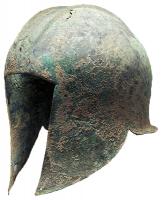 CSQ-3012 - Casque de type gréco-illyrienbronzeCasque en tôle, avec l'emplacement du visage dégagé par une découpe rectangulaire entre deux couvre-joues formant une pointe de part et d'autre du menton; parfois des côtes parallèles au-dessus du front et une sorte de renfort en forme de crête dans l'axe du timbre; couvre-nuque peu débordant, en angle doit.