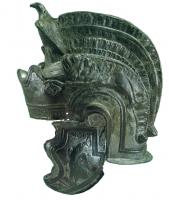 CSQ-4011 - Casque d'équipement sportifbronzeCasque en tôle emboutie, caractérisé par de forts reliefs figurant divers éléments et ornements : le casque comporte une sorte de diadème frontal au-dessus duquel émerge un cimier de plumes en haut-relief, éventuellement terminé vers l'avant par une figure d'aigle; deux lions sont étendus sur les côtés; des aigles tenant une couronne dans leur bec ornent également les paragnathides. Etamage.