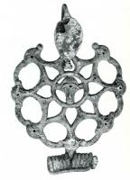 FIB-3892 - Fibule laténienne à décor plastiquebronzeFibule de schéma laténien, à pied redressé en forme de plaque ovale, terminée par un bouton bifide; l'arc est remplacé par un motif circulaire ajouré, formant des motifs symétriques autour d'une tête humaine de face, coiffée de deux crosses.