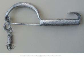 FIB-3912 - Fibule de type BaškaargentFibule de grande taille, à arc massif ou ouvert par dessous, ressort unilatéral à deux spires, pied plat et allongé, prolongé pat un ornement terminal redressé vers l'arc, en forme de langue.