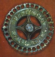 FIB-41089 - Fibule circulaire émailléebronzeFibule circulaire émaillée comportant une couronne émaillée, bordée de festons ajourés d'une succession de trous formant une dentelle périphérique; au centre, un carré à côtés concaves est également émaillé, et orné d'un rivet central surélevé lui aussi émaillé.