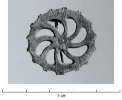FIB-41250 - Fibule circulaire à décor rayonnantbronzeFibule plate, constituée d'un motif rayonnant ajouré; petits ergots sur le pourtour, cercle pointé au centre. Articulation par ressort sur plaquette(s).