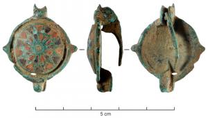 FIB-41439 - Fibule émaillée / Umbonate BroochbronzeFibule de forme générale circulaire, le corps occupé par un umbo formant un fort relief arrondi, entièrement couvert d'une ou de plusieurs rangées concentriques d'émaux disposés en loges triangulaires, souvent alternées bleues et rouges, autour d'un bouton central incrusté d'émail ou d'une bille de verre. Sur le pourtour, un bouton eou disque, et un anneau, diamétralement opposés, parfois une bordure rayonnante de cercles oculés séparés par des lignes concaves).