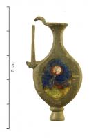 FIB-41479 - Fibule skeuomorphe : cruchebronzeFibule en forme de cruche à anse surélevée : le contenu est matérialisé par une zone ovale émaillée, creusée dans le corps de la broche, avec des inclusions de verre ; bouton mouluré à la base; au revers, articulation à charnière sur deux plaquettes.