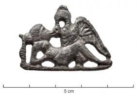 FIB-41595 - Fibule zoomorphe, groupe : Leda et le cygnebronzeFibule en relief plat, les détails indiqués par des incisions: Leda, couchée sur le dos, appuyée sur un coude, s'unit au cygne qui l'embrasse en déployant ses ailes.