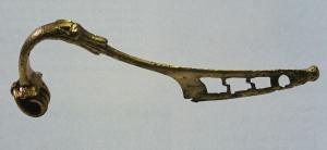 FIB-41639 - Fibule à plaquettes et tête de canidébronzeType à arc non interrompu, effilé, coudé à la tête, de section variable (ronde, semi-circulaire, plate...); ressort à 6 ou 8 spires, corde externe, retenue par une griffe et protégé sur le dessus par des 