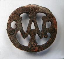 FIB-41774 - Fibule au nom de MARSbronzeBroche circulaire plate, sur laquelle une série d'ajours découpent les lettres M, A et R (M et A ligaturés). Le contour externe forme la lettre O. Cercles oculés dans les intervalles. Au revers, ressort sur plaquette unique.