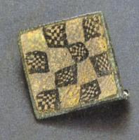 FIB-4540 - Fibule carrée émaillée en millefioribronzeFibule carrée dont l'arc plat creusé d'une grande loge reçoit un décor en damier de millefiori. Au revers, articulation à charnière par deux plaquettes soudées.